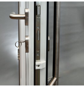 Detalhe de fecho multiponto GU com cilindro de segurança, chave inserida e puxador muleta inox em porta de PVC abertura direita
