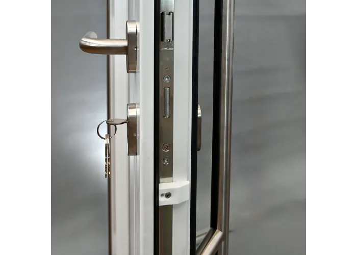 Detalhe de fecho multiponto GU com cilindro de segurança, chave inserida e puxador muleta inox em porta de PVC abertura direita
