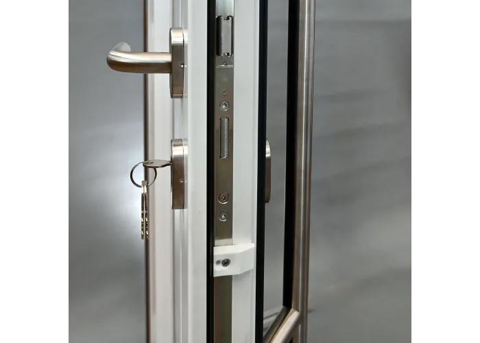 Detalhe de fecho multiponto GU com cilindro de segurança, chave inserida e puxador muleta inox em porta de PVC abertura direita